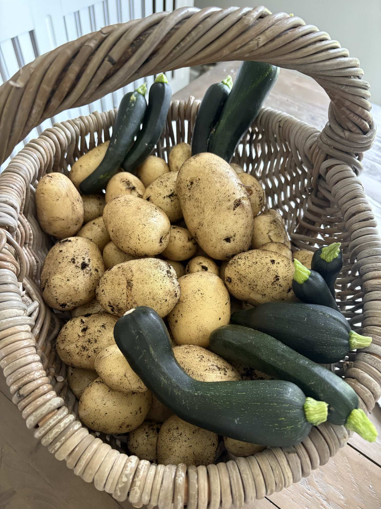 A wicker basket of just-dug potatoes and courgettes.